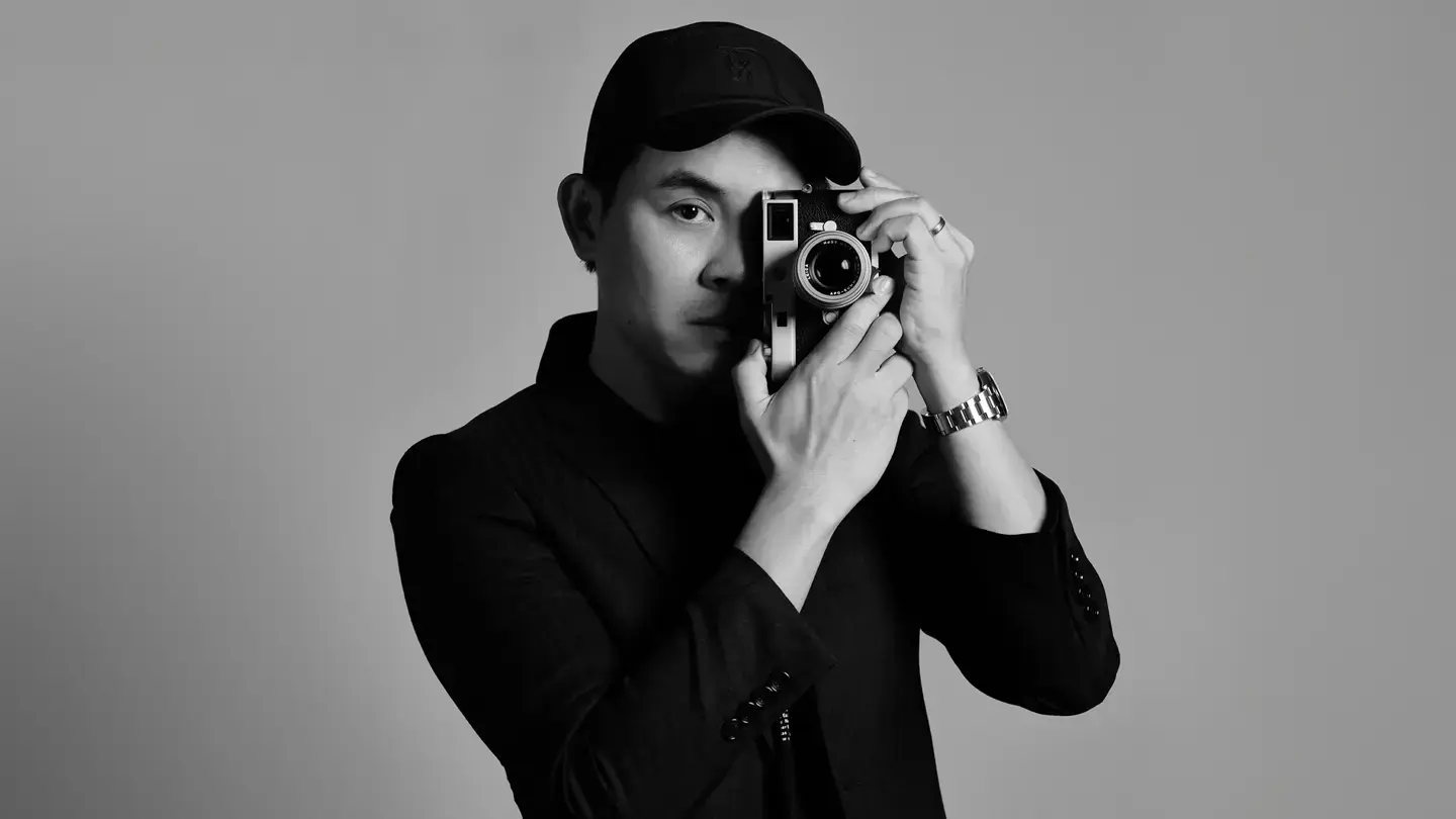 A photographer focusing the Leica M11 rangefinder by hand, in black and white