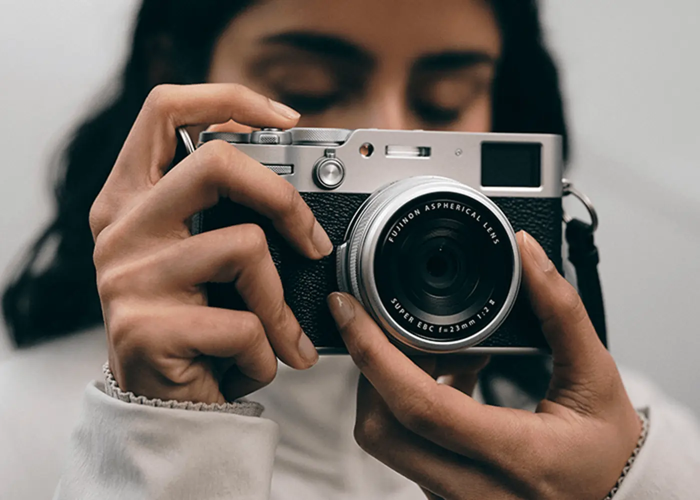 A traveller raising the Fujifilm X100VI compact camera to their eye on a city street
