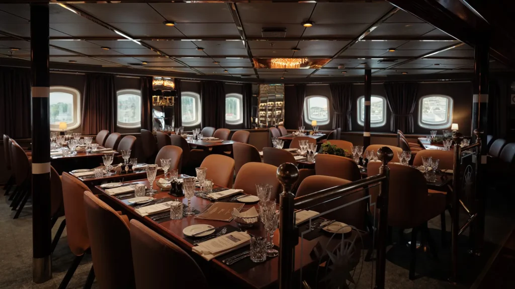 The dining saloon aboard MS Vesteralen, tables laid beside portholes