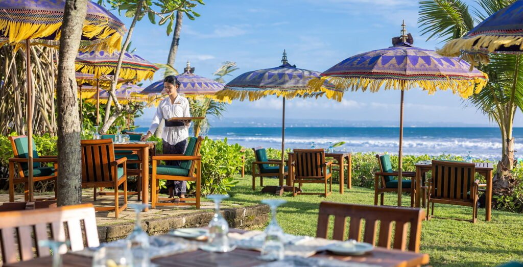 Tables under Balinese parasols on the lawn at The Oberoi, Bali, looking out to the beach at Seminyak