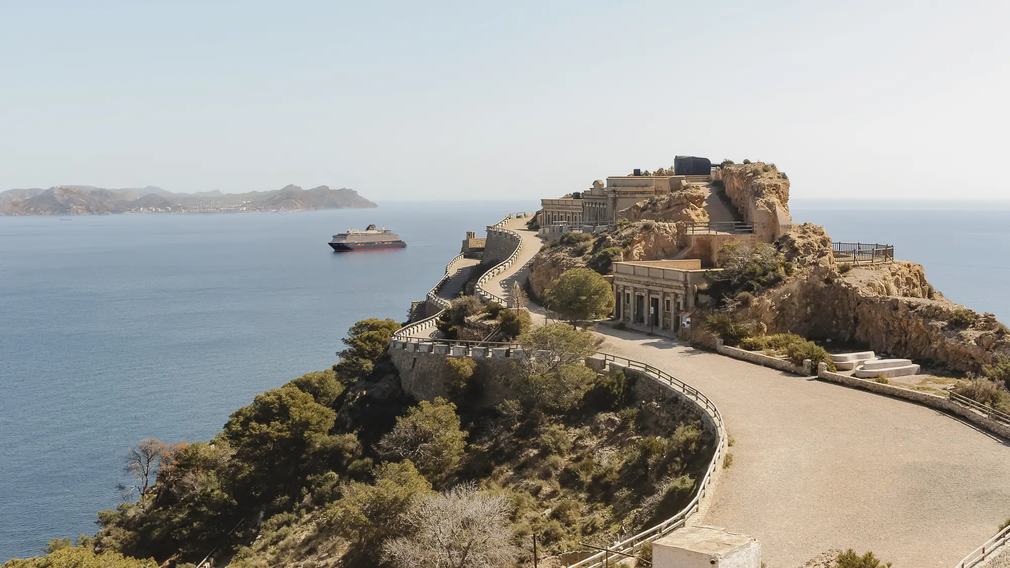 A clifftop headland with an Explora ship offshore in the Mediterranean