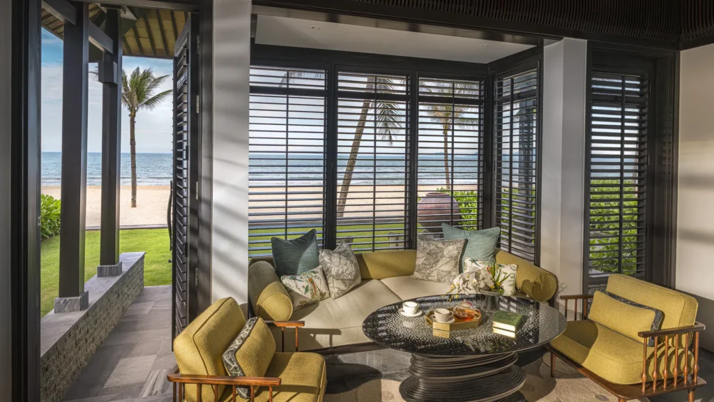 A seating area in a renovated Signature villa at The Nam Hai opening through folding doors towards Ha My Beach