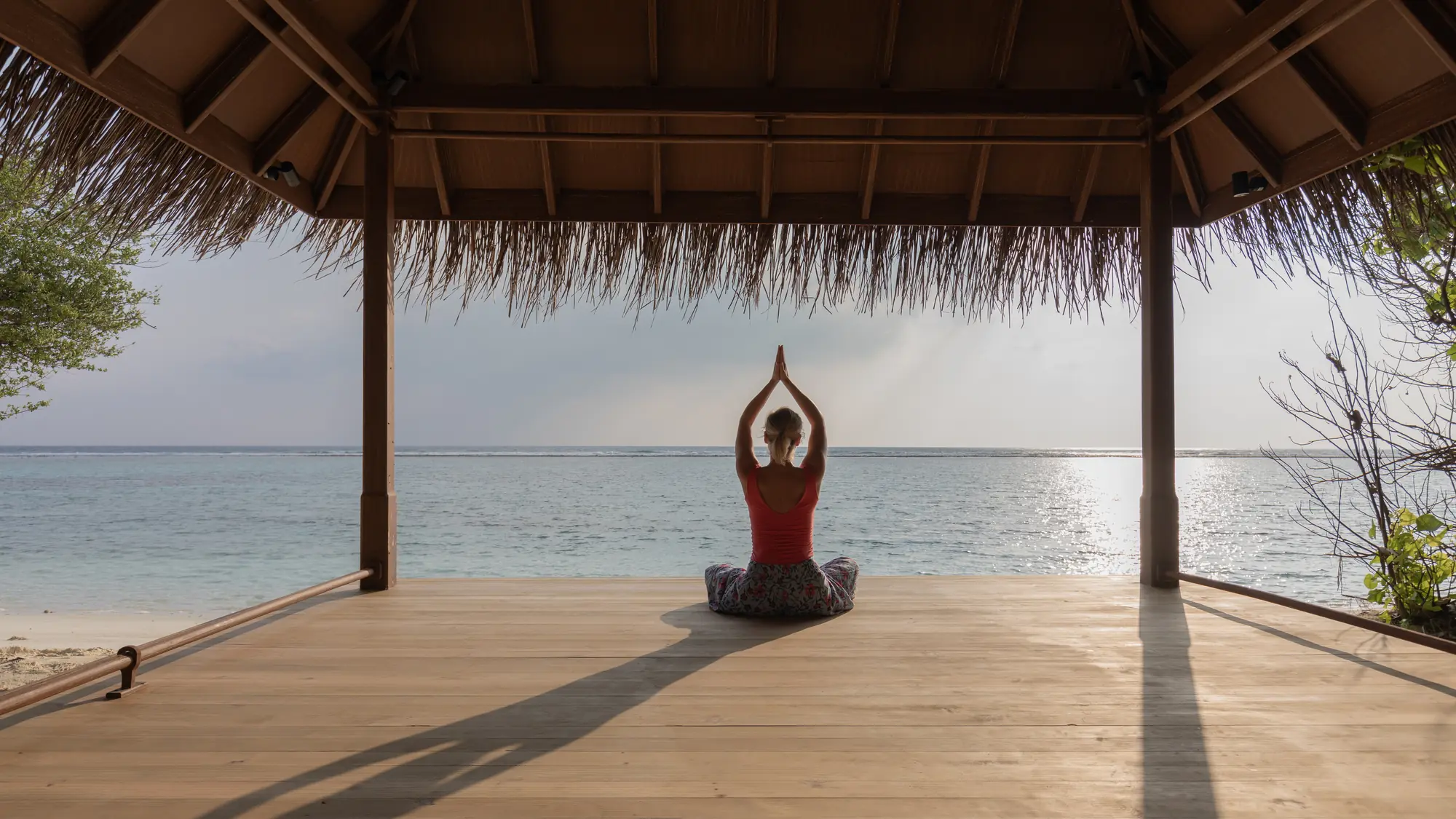 A woman in seated yin yoga practice in the open beach pavilion at Six Senses Kanuhura, facing the Indian Ocean