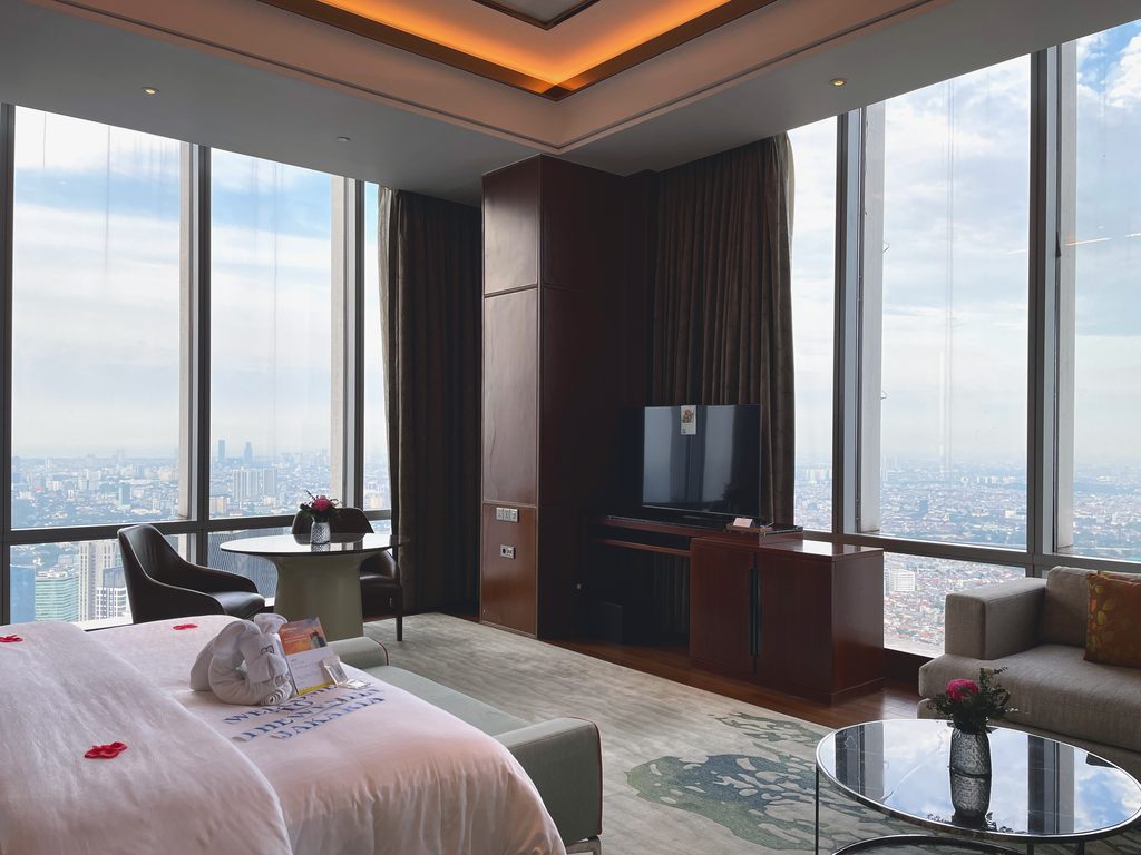 The Ambassador Suite bedroom on the 66th floor, the Jakarta skyline filling the corner windows — The Westin Jakarta