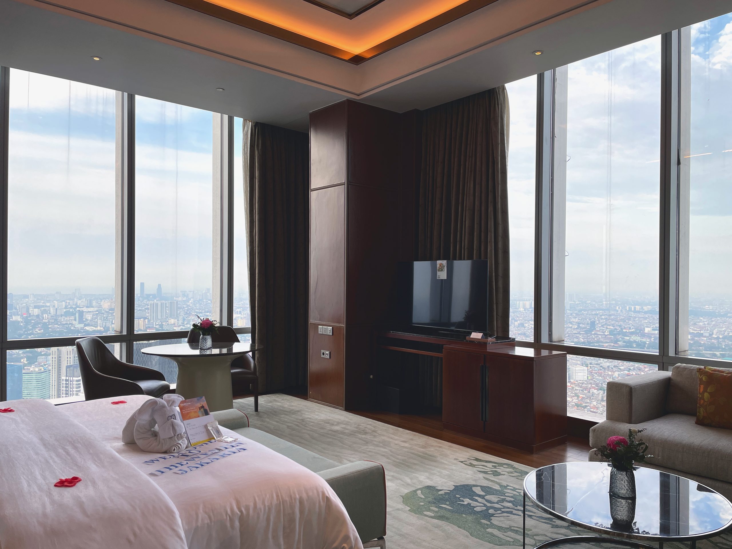 The Ambassador Suite bedroom on the 66th floor, the Jakarta skyline filling the corner windows — The Westin Jakarta