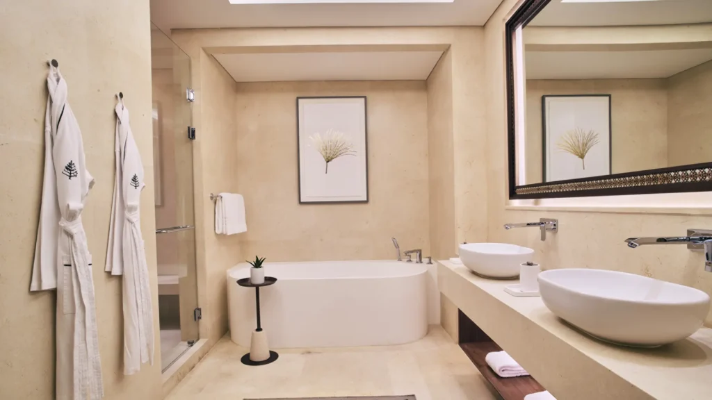 Marble bathroom in the two-bedroom residential suite, with a freestanding bathtub, twin vessel basins and robes hanging by the shower