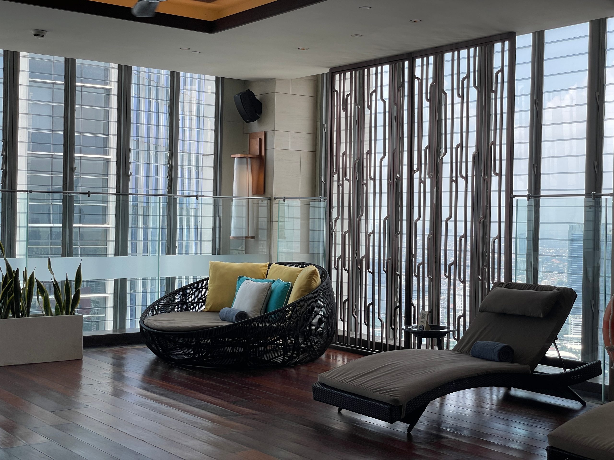 Loungers set against the pool's window wall — The Westin Jakarta