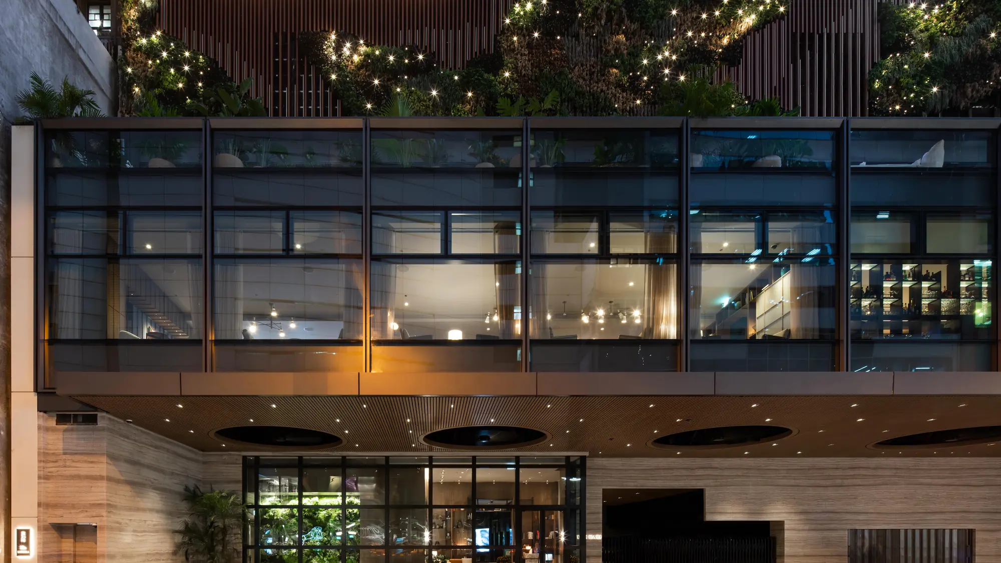 The lit exterior of The Hari Hong Kong in Wan Chai at night, planting running along its upper terrace