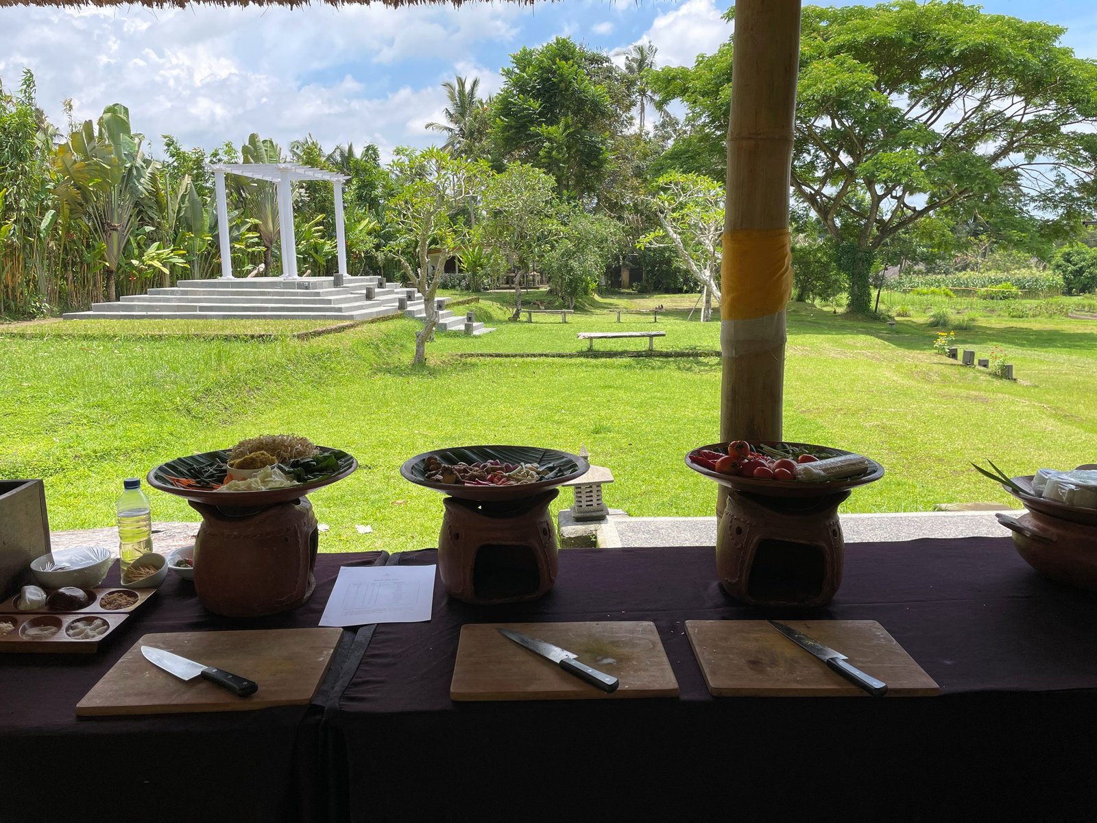 Cooking stations laid with knives, boards and clay stoves in the pavilion at Visesa Ubud, facing the lawn