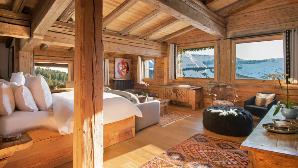 Chalet-style suite with exposed timber beams, a bed and windows onto snowy mountains