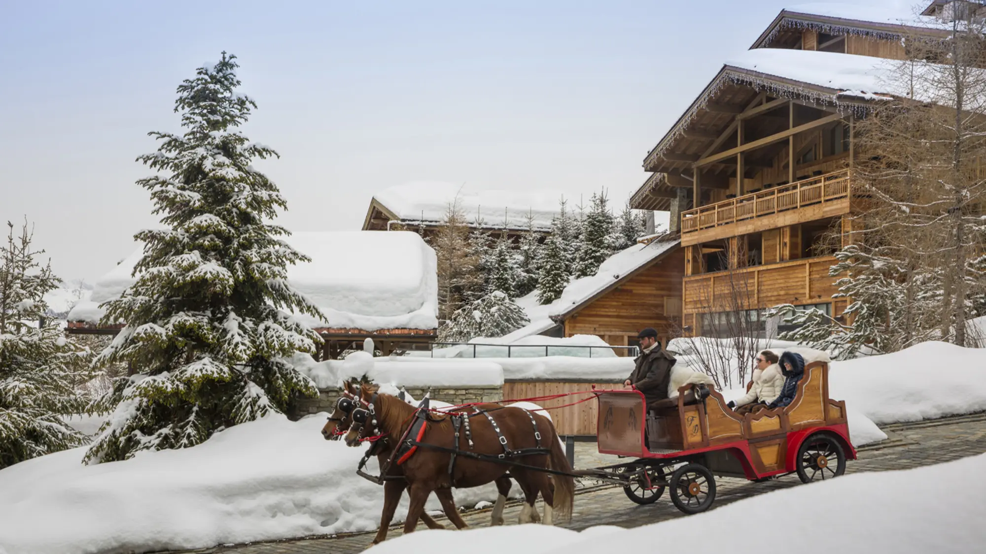 A horse-drawn carriage on a snowy lane beside wooden chalets in Megève