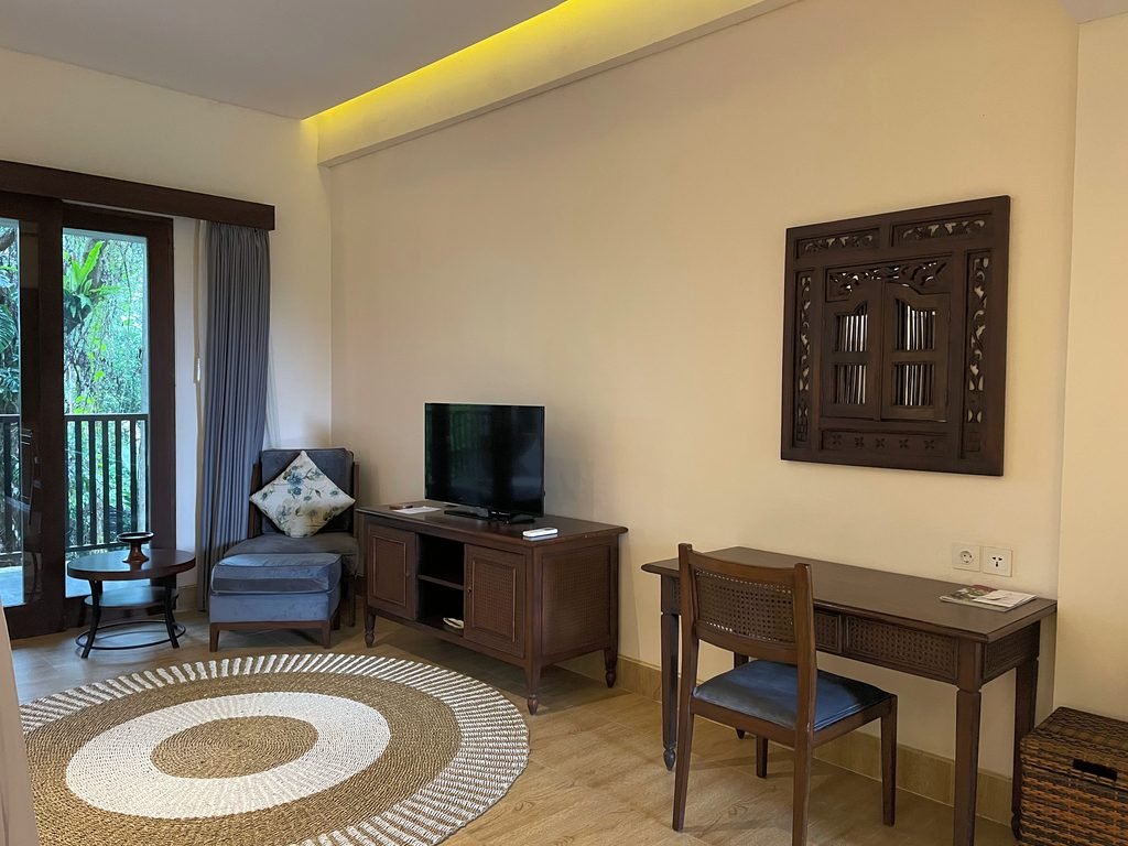 The desk, television and armchair in the Jungle Suite at Visesa Ubud, with the balcony doors open