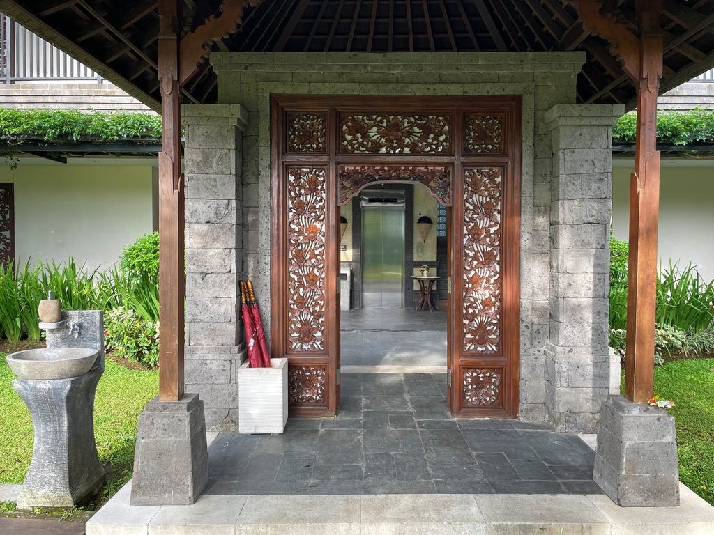The carved timber entrance to a suite building at Visesa Ubud, with a stone basin beside it