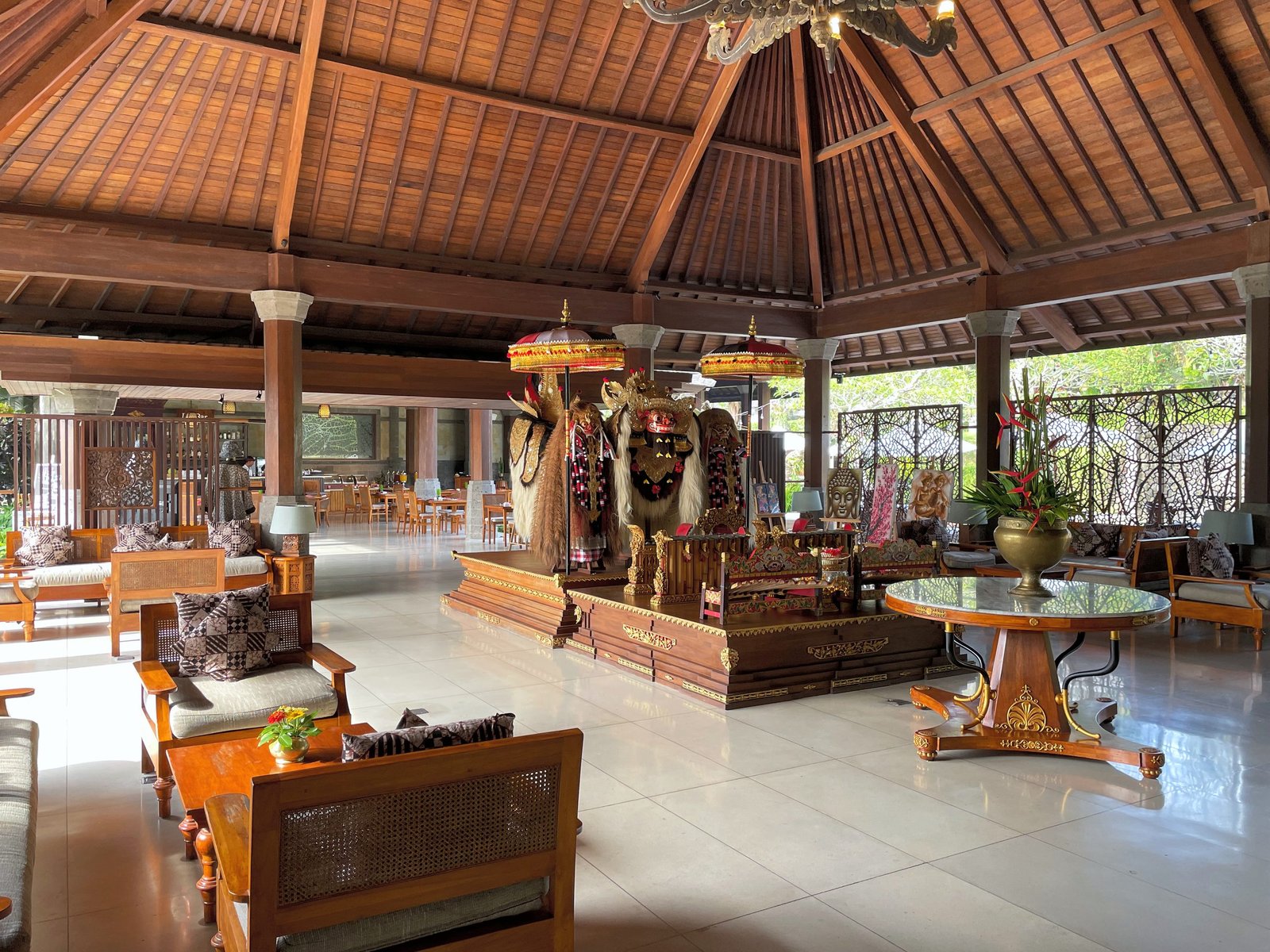 The open lobby pavilion at Visesa Ubud, with teak seating, a Barong figure and a gamelan