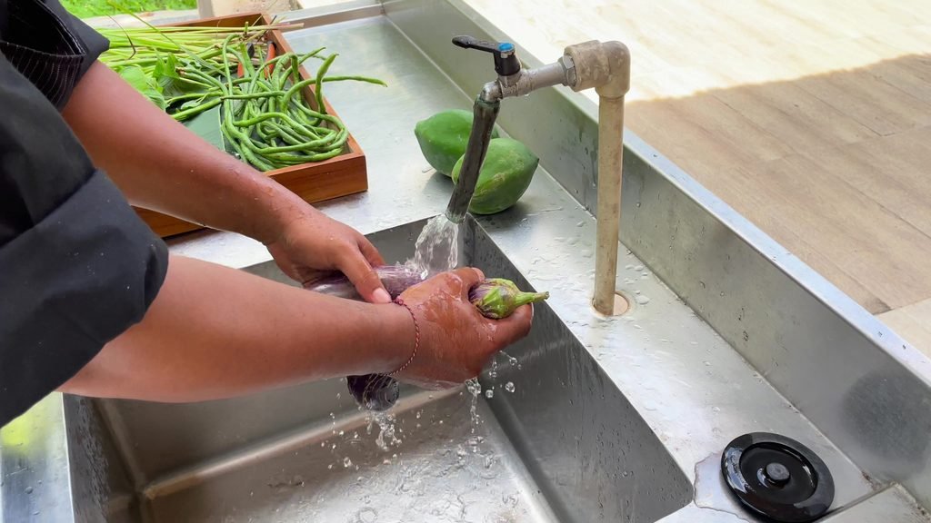Freshly picked aubergine and long beans being washed at a sink beside the farm at Visesa Ubud