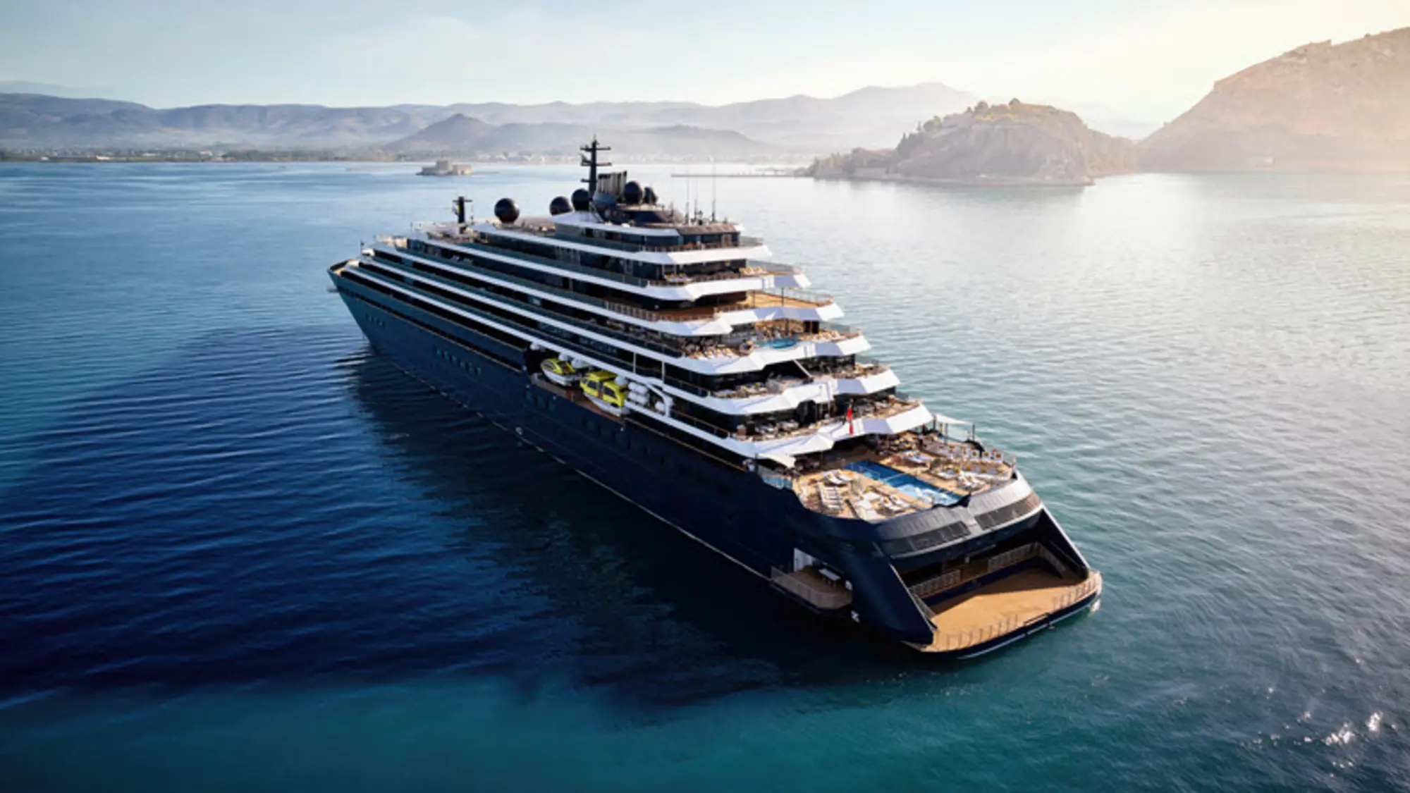 The Ritz-Carlton yacht Evrima at anchor in a calm bay with hills behind