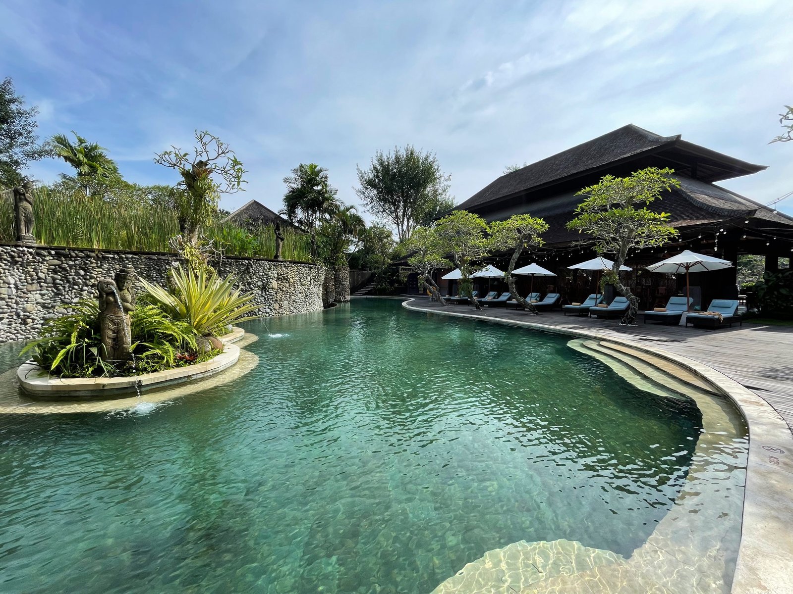 The free-form swimming pool at Visesa Ubud curving around a planted island, with the restaurant pavilion behind