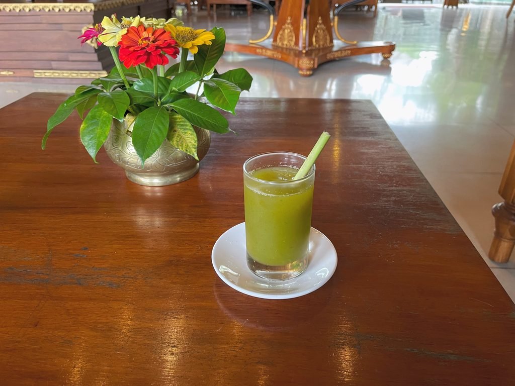 A green welcome drink with a lemongrass stirrer beside a bowl of zinnias at Visesa Ubud