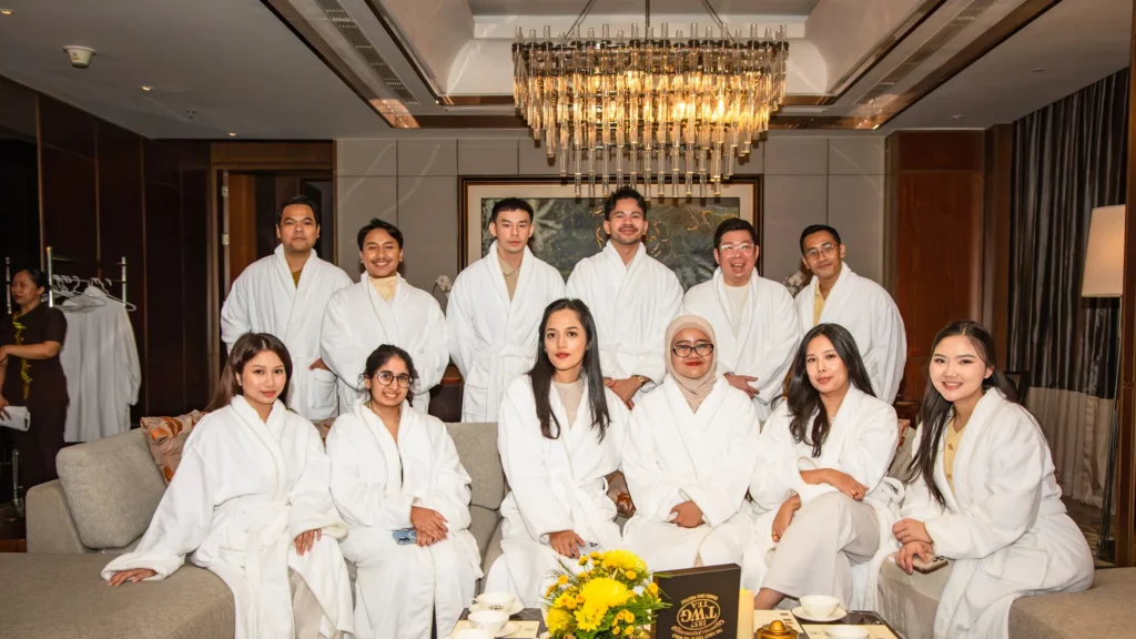 Guests in white bathrobes posing together on a sofa beneath a crystal chandelier in the Presidential Suite
