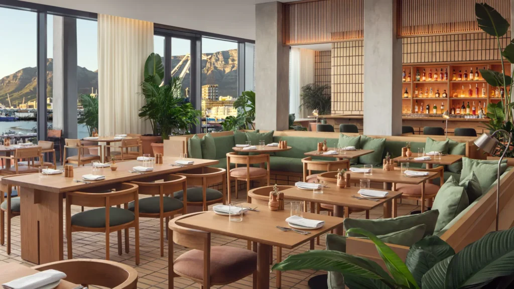 Restaurant with timber tables, green banquettes and floor-to-ceiling windows towards the mountains