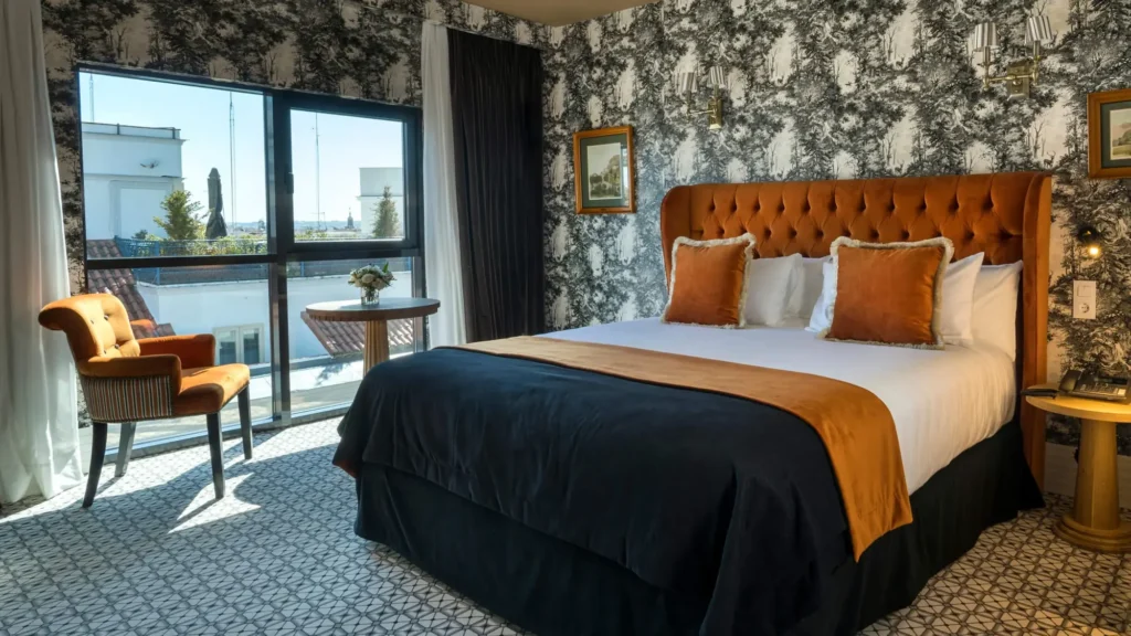 Guest room with a tufted orange headboard, botanical wallpaper and a window over central Madrid
