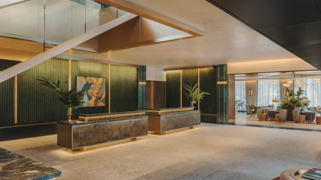 Hotel lobby with green fluted wall panels, stone reception desks and a white sculptural staircase