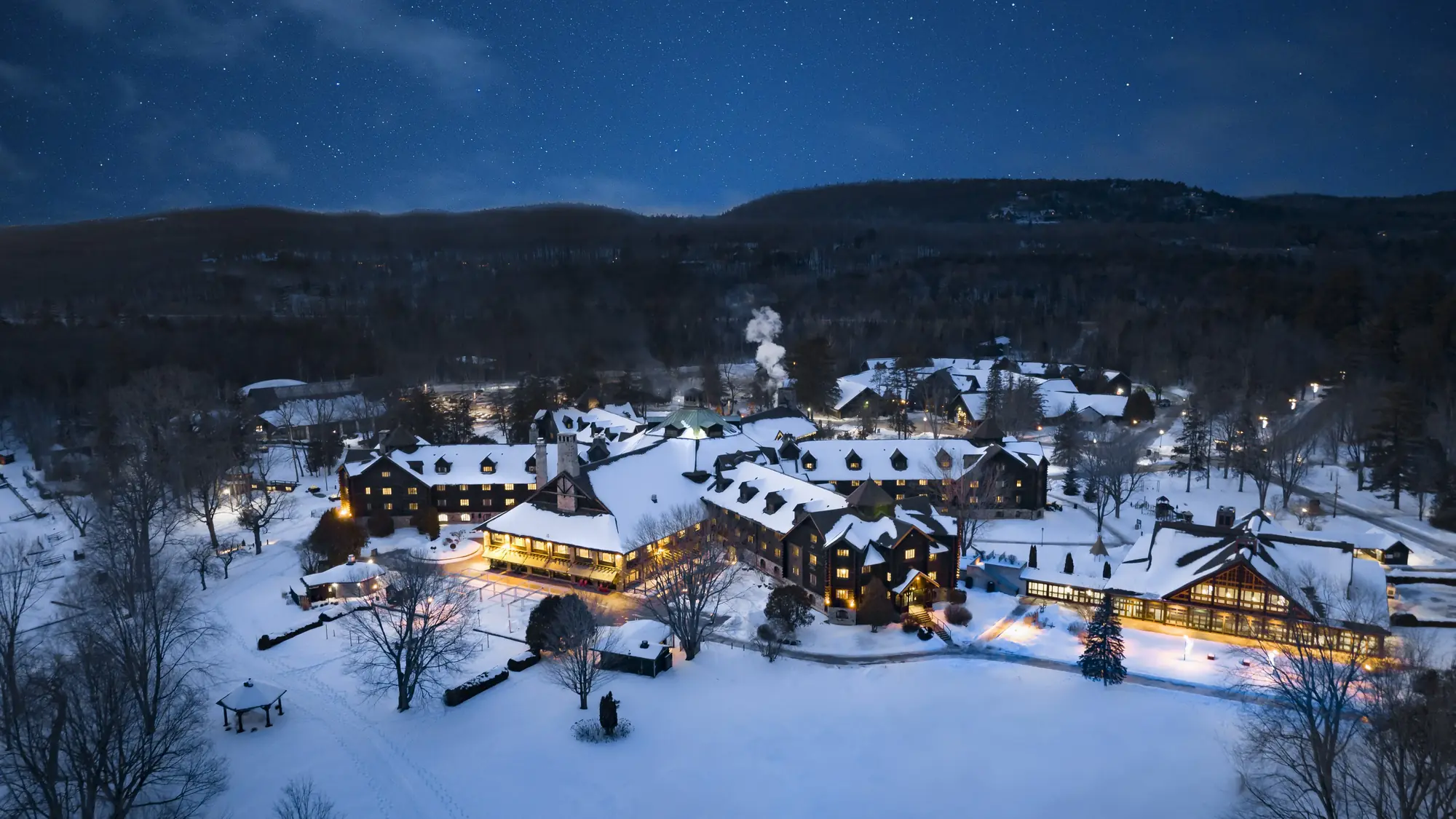 Aerial night view of a snow-covered resort of timber lodges with lit windows under a starry sky