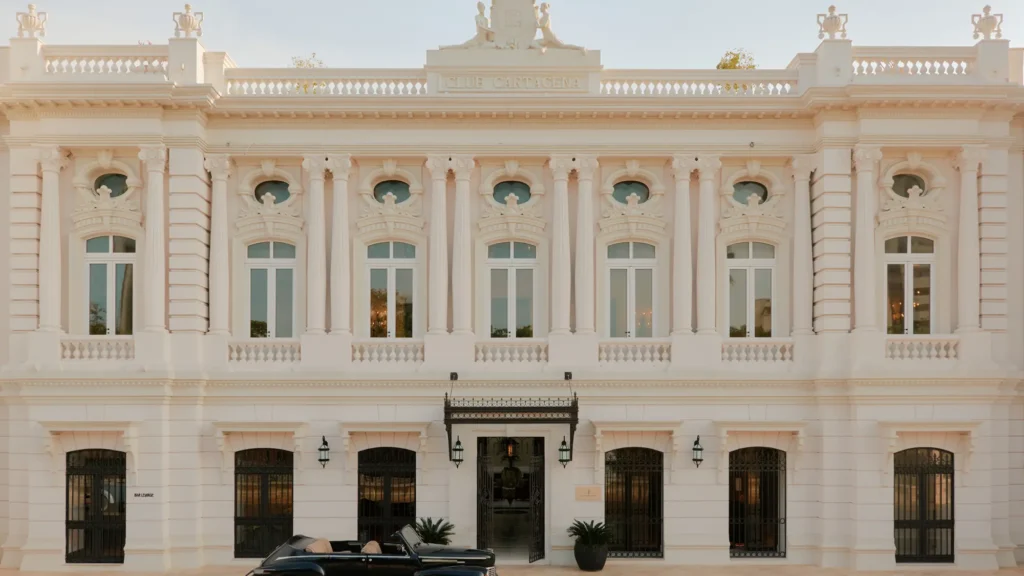 Restored white colonial façade with arched windows and a vintage black car at the entrance