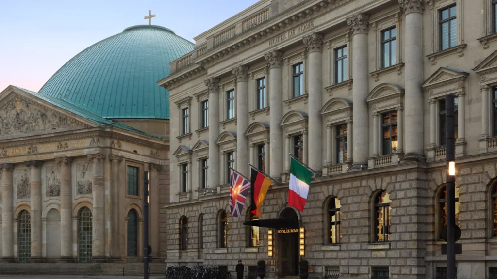 Historic stone façade with flags beside the green dome of St. Hedwig's Cathedral, Berlin
