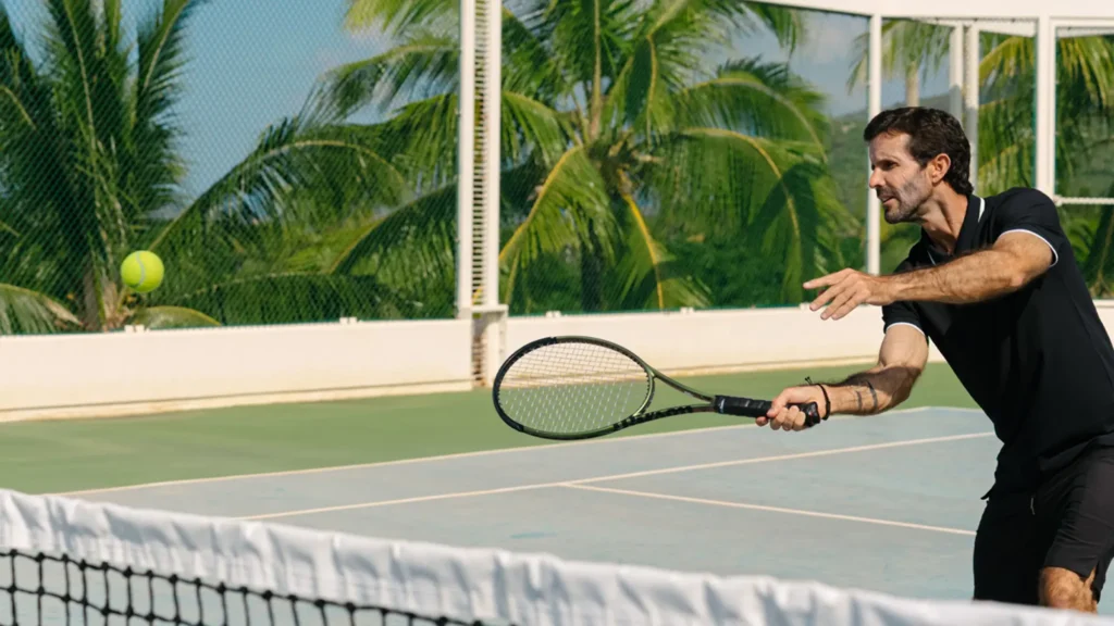 A man reaching for a forehand volley at the net on a palm-fringed tennis court
