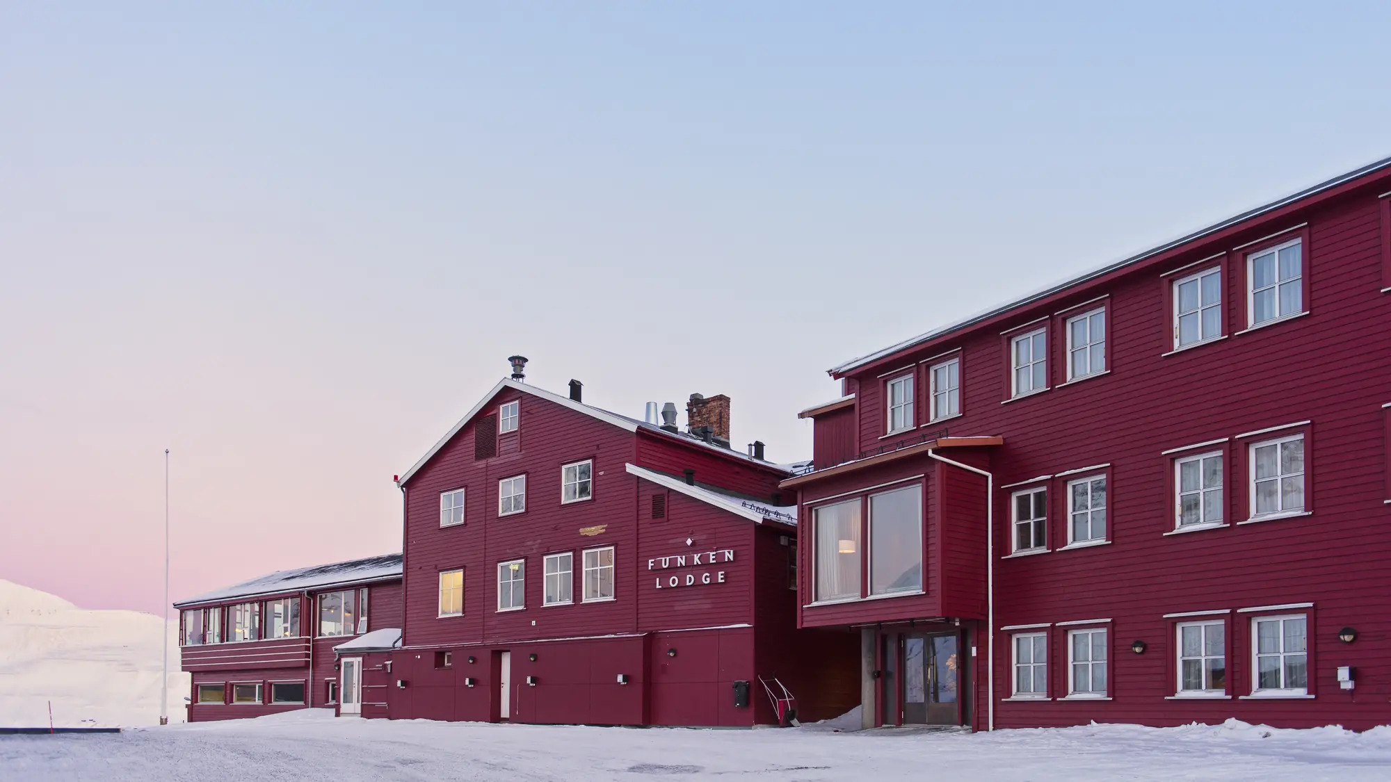 Red wooden Funken Lodge building in snow under a pale pink polar sky in Longyearbyen, Svalbard