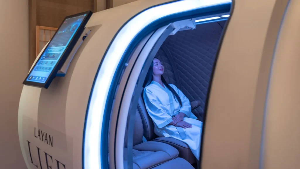 Guest in a robe reclining inside an illuminated Layan Life wellness pod