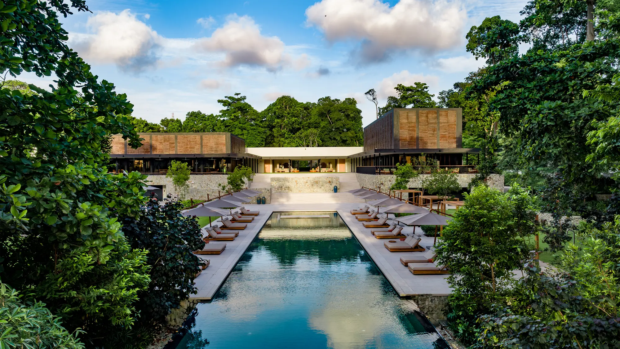 Long outdoor pool lined with sun loungers and surrounded by rainforest at Mandarin Oriental, Desaru Coast