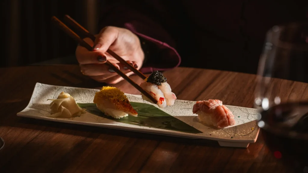Nigiri sushi topped with caviar on a long ceramic plate, picked up with chopsticks