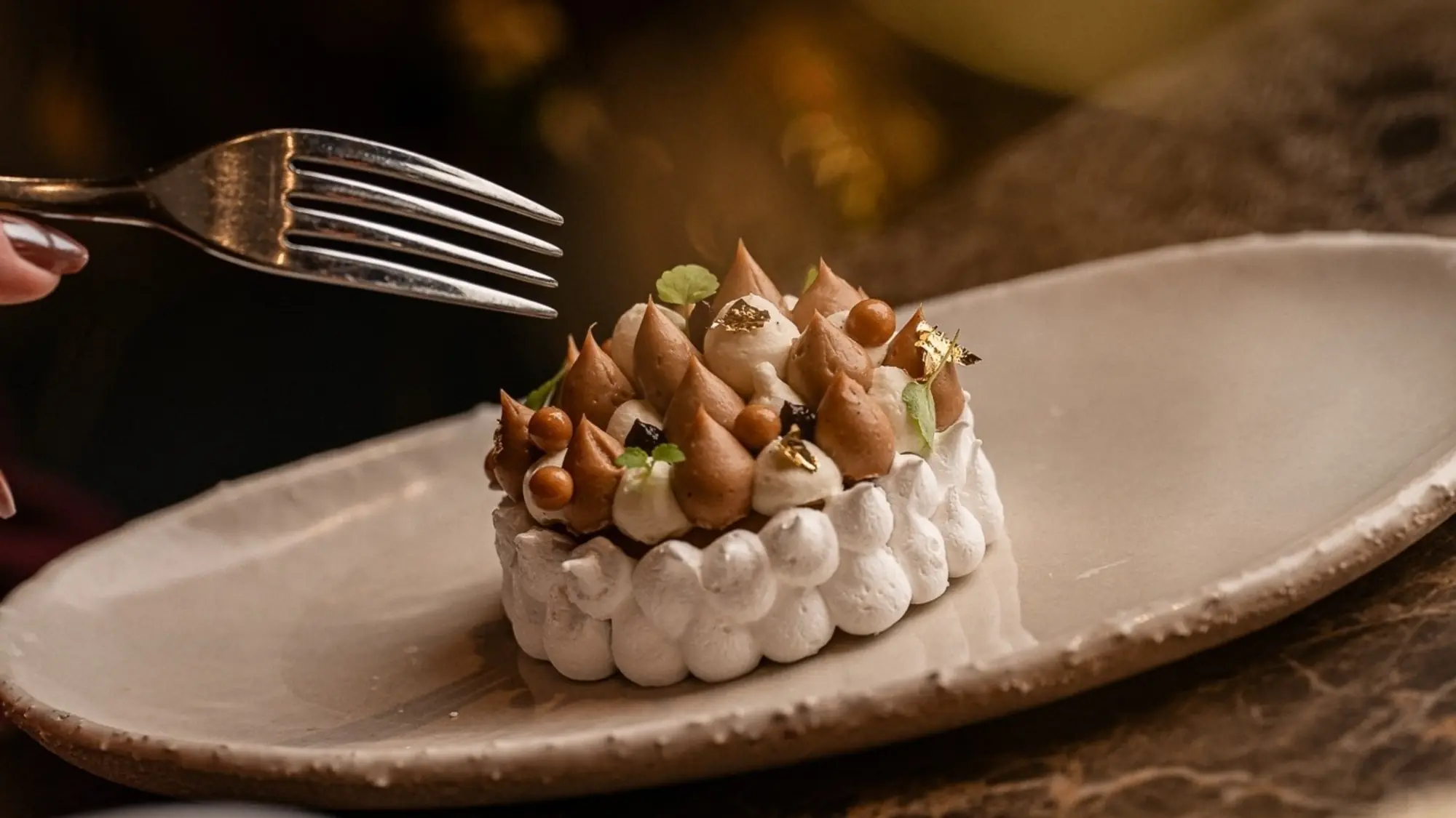 Round meringue dessert topped with piped chestnut-coloured cream on a pale ceramic plate