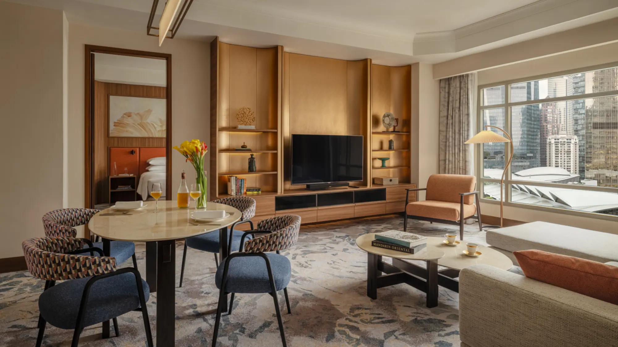 Apartment living room with round dining table, wood shelving, sofa and a window onto city towers