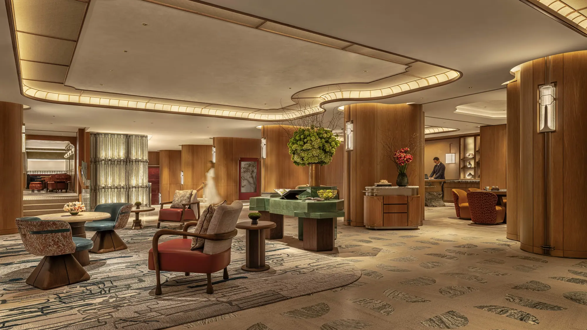 Hotel interior with curved timber-clad columns, a patterned carpet, armchairs and a green stone desk