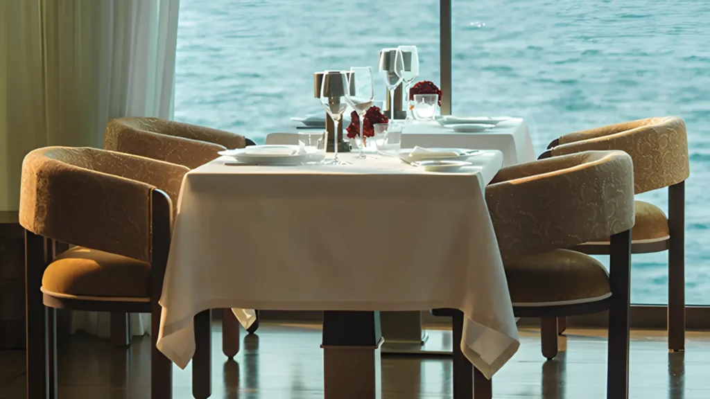 Dining tables with white cloths and curved armchairs in front of a sea view