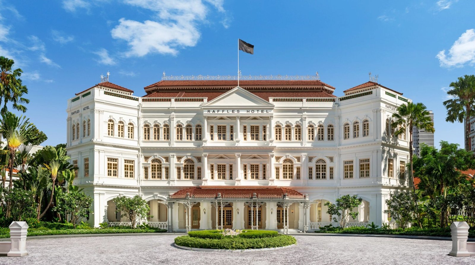 The white colonial facade of Raffles Singapore behind its front lawn and palms