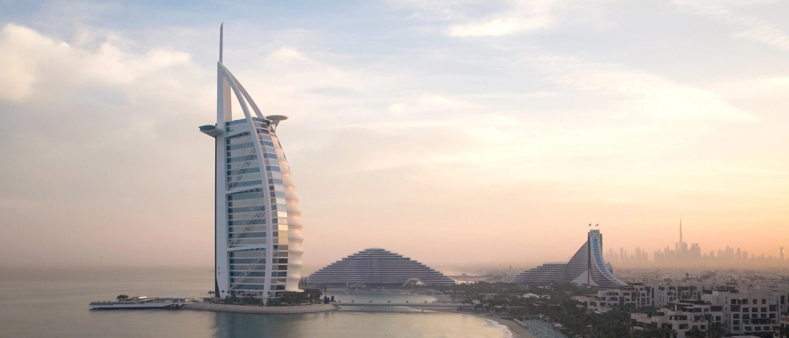 Burj Al Arab at dusk beside Jumeirah Beach Hotel, with the Dubai skyline behind