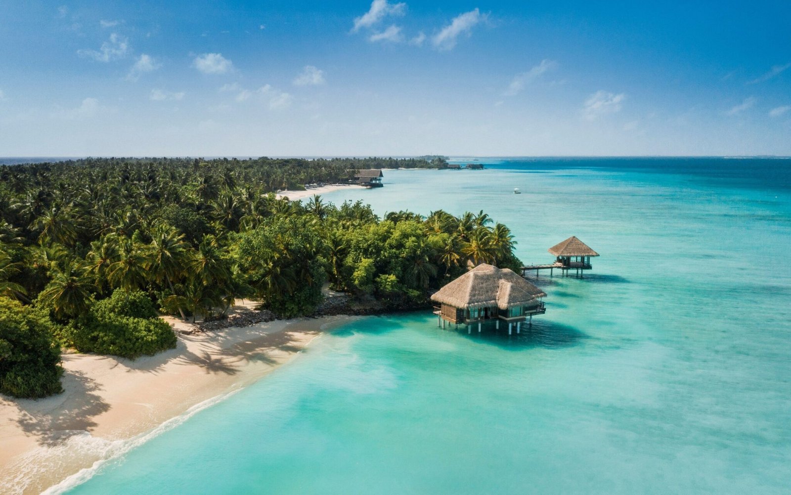 Aerial view of One&Only Reethi Rah's palm-covered shore and overwater pavilions