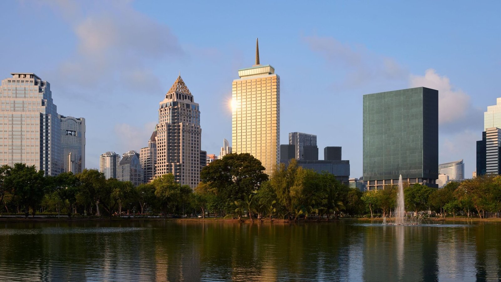 The gold tower and spire of Dusit Thani Bangkok above Lumpini Park lake