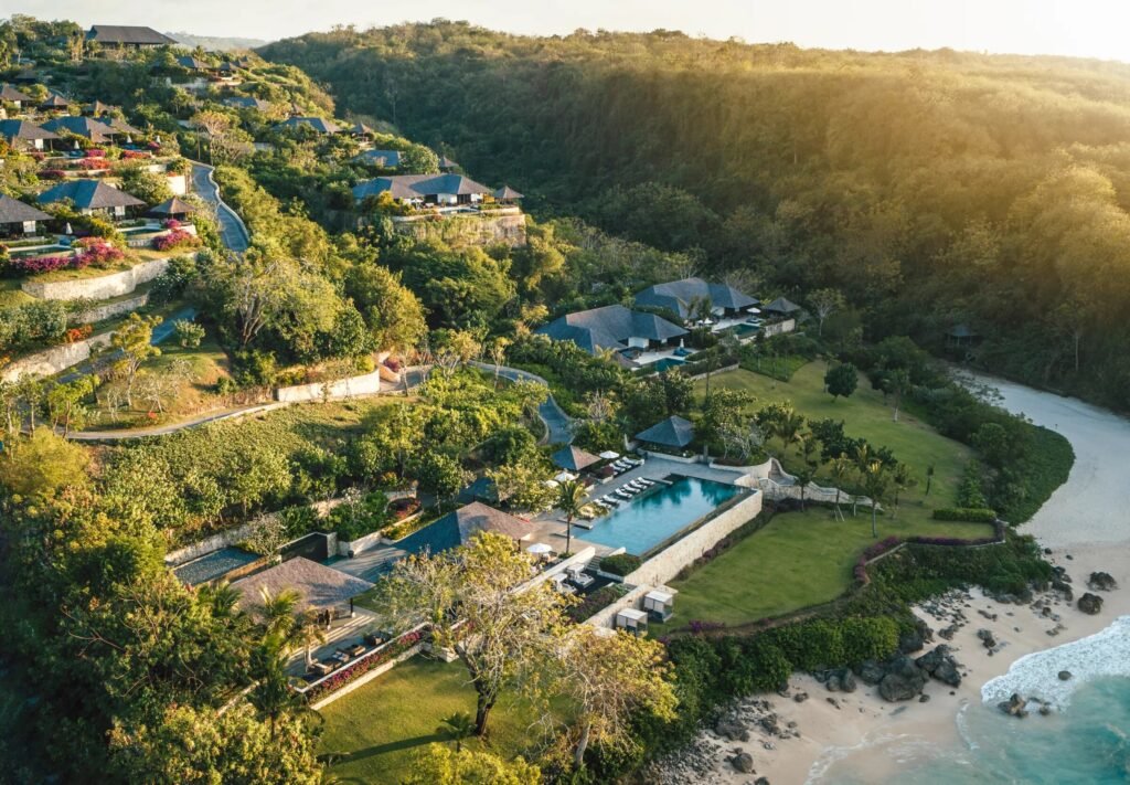 Raffles Bali from the air, villas stepping down a green hillside to the main pool and the beach at Jimbaran
