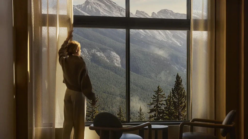A guest opening the curtains on a mountain view at Rimrock Banff