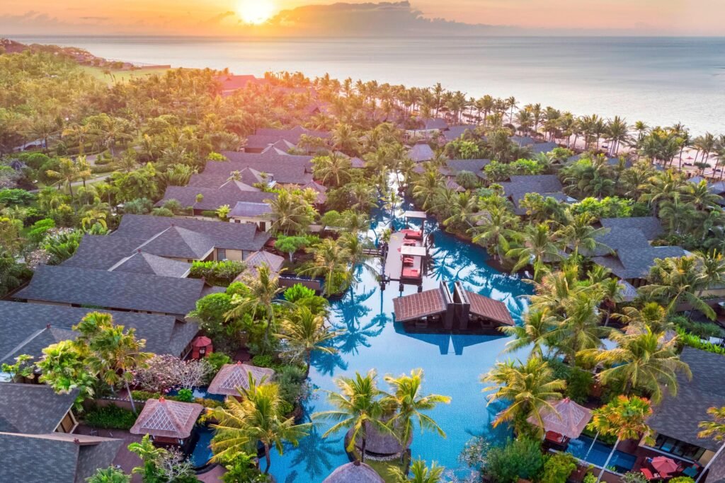 The St. Regis Bali Resort from the air at sunset, its lagoon pool winding between the villas towards the beach at Nusa Dua