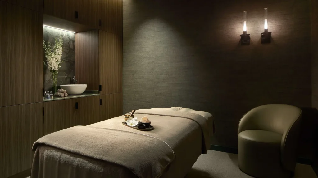 Treatment room with a massage table, armchair and wood-panelled walls at the Tivoli Wellness Club, Milan