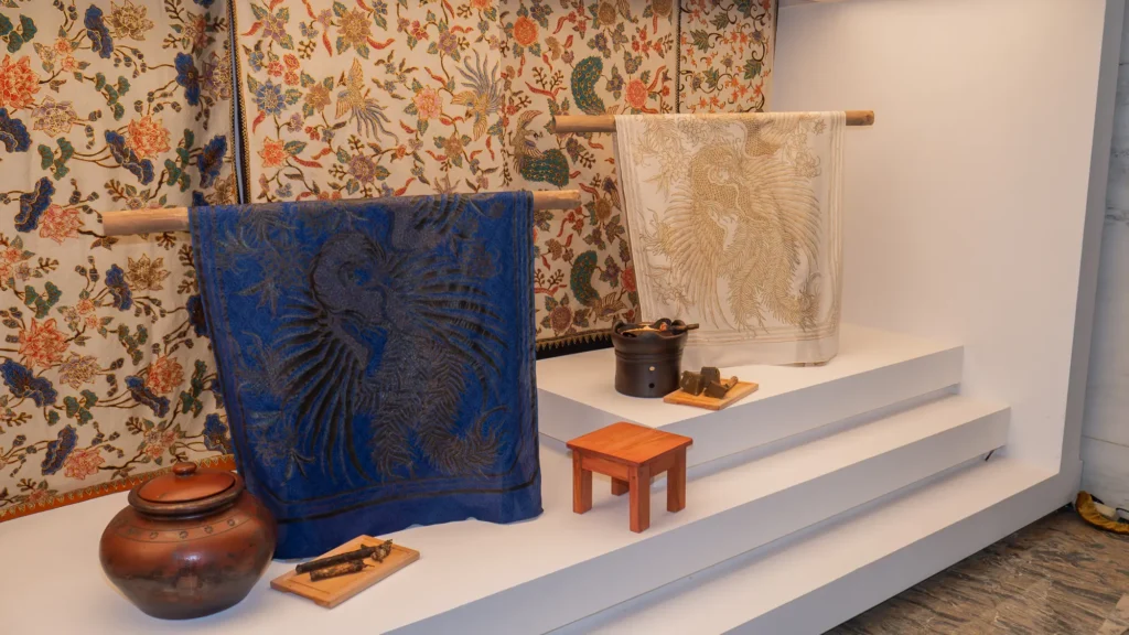 Indigo and cream batik cloths with bird motifs draped over bamboo rails in front of a floral batik wall