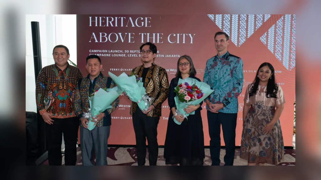 Six people in batik and formal dress, three holding bouquets, in front of a Heritage Above The City launch backdrop